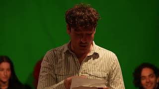 a man on stage reading from a sheet of paper